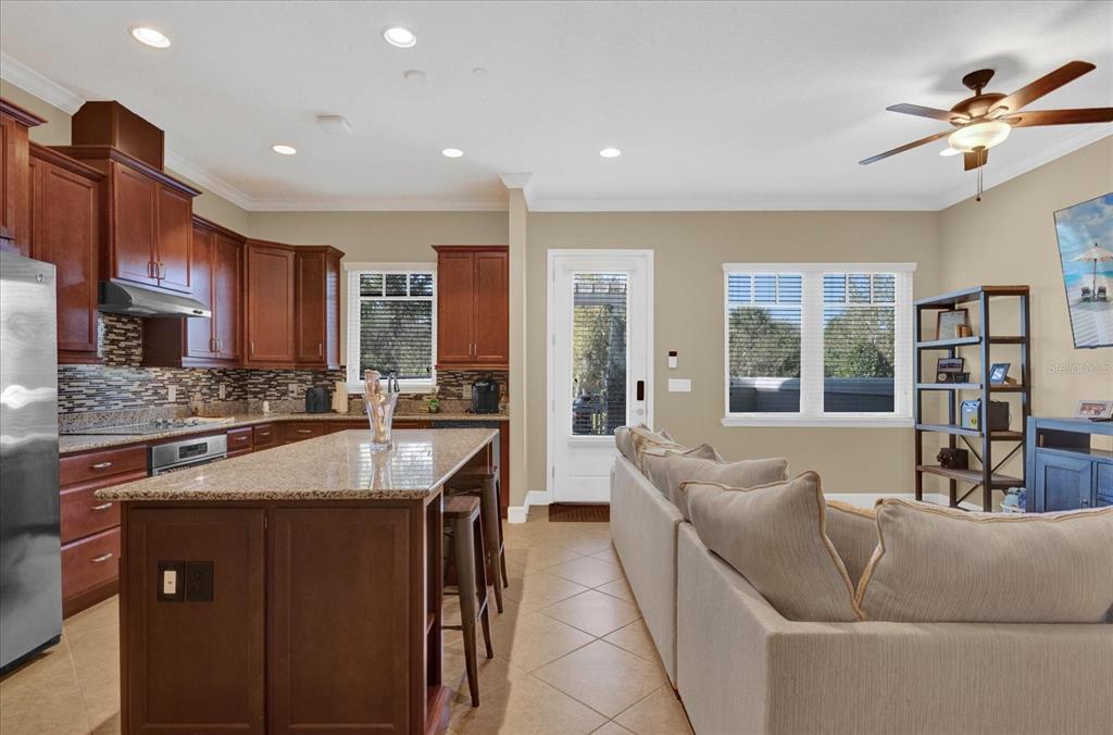 A kitchen with wood cabinets and granite countertops opens to a living area with seating — 9219 LAUREATE BOULEVARD, ORLANDO, FL