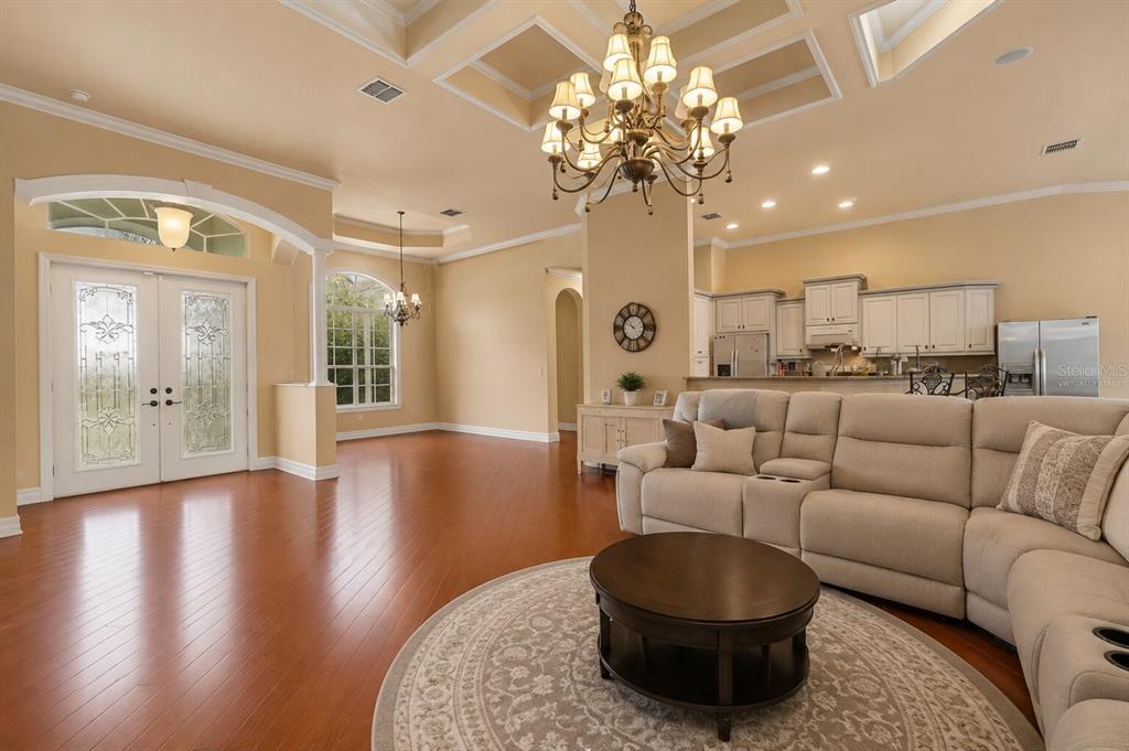A spacious living room features a large leather sectional, a chandelier, and hardwood flooring — 20831 COPPERHEAD DRIVE, LEHIGH ACRES, FL