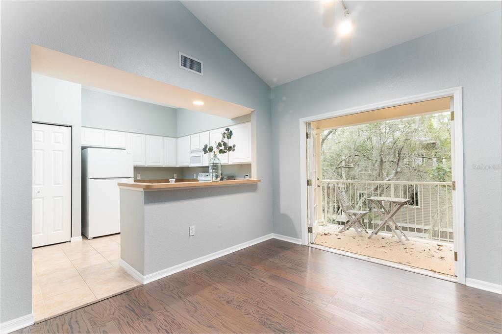 A dining area with wood floors opens to a kitchen and a balcony with outdoor seating — 4850 SW 91ST TERRACE UNIT 301, GAINESVILLE, FL