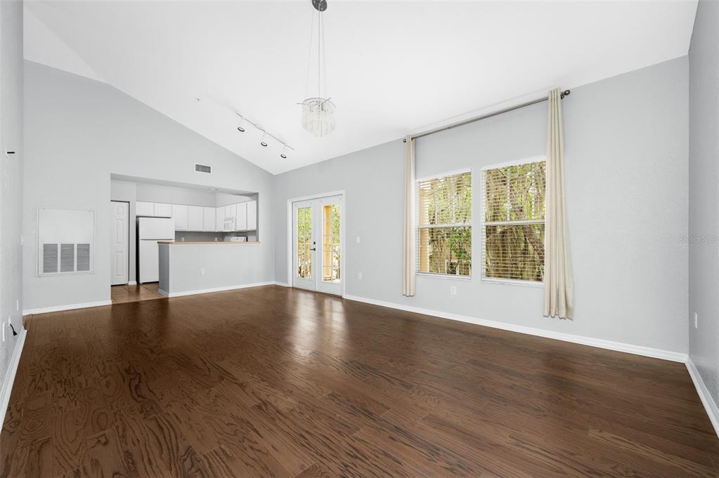 An empty living room with hardwood floors, vaulted ceilings, and an open kitchen — 4850 SW 91ST TERRACE UNIT 301, GAINESVILLE, FL