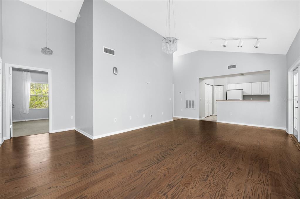A spacious living room with high ceilings, hardwood floors, and an adjacent kitchen area — 4850 SW 91ST TERRACE UNIT 301, GAINESVILLE, FL