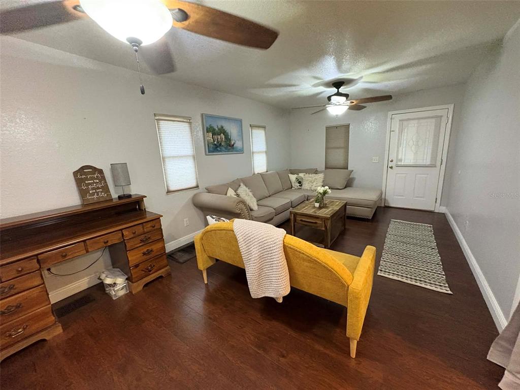 A living room features a yellow sofa, a sectional, a wooden desk, and dark flooring — 1040 S OHIO AVE, LAKELAND, FL