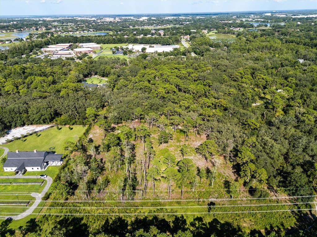 An aerial view shows a wooded lot next to a building with a gray roof — MARKHAM WOODS ROAD, LAKE MARY, FL