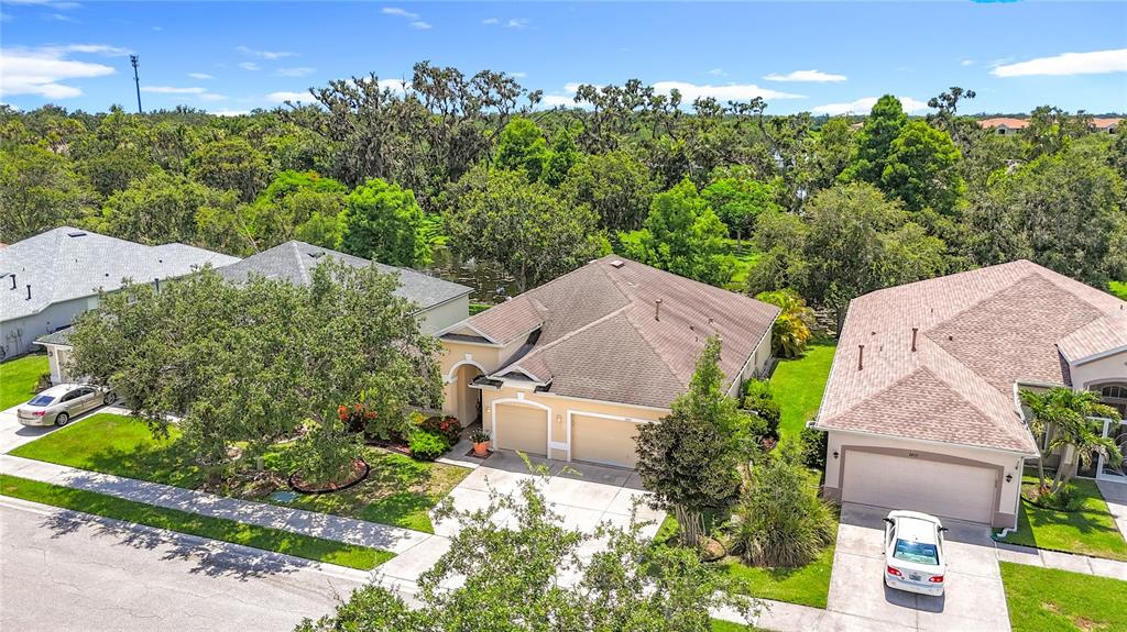 An aerial view shows three suburban houses with driveways and garages near a wooded area — 3409 61ST TERRACE E, ELLENTON, FL