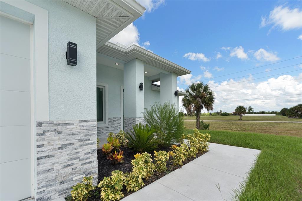 A light blue house exterior features stone veneer, modern wall sconces, and a concrete walkway — 13 TEAK LANE, PLACIDA, FL