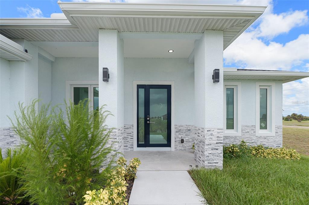 The front entrance of a modern house features a dark glass door and stone siding — 13 TEAK LANE, PLACIDA, FL
