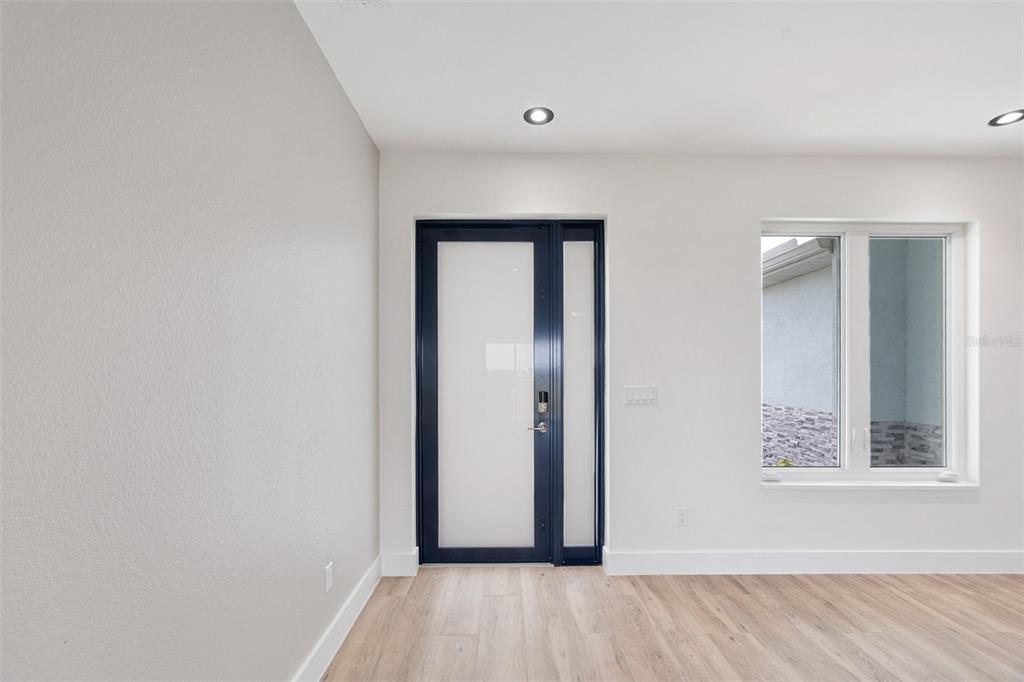 An interior room with light wood flooring, white walls, a dark-framed glass door, and a window — 13 TEAK LANE, PLACIDA, FL