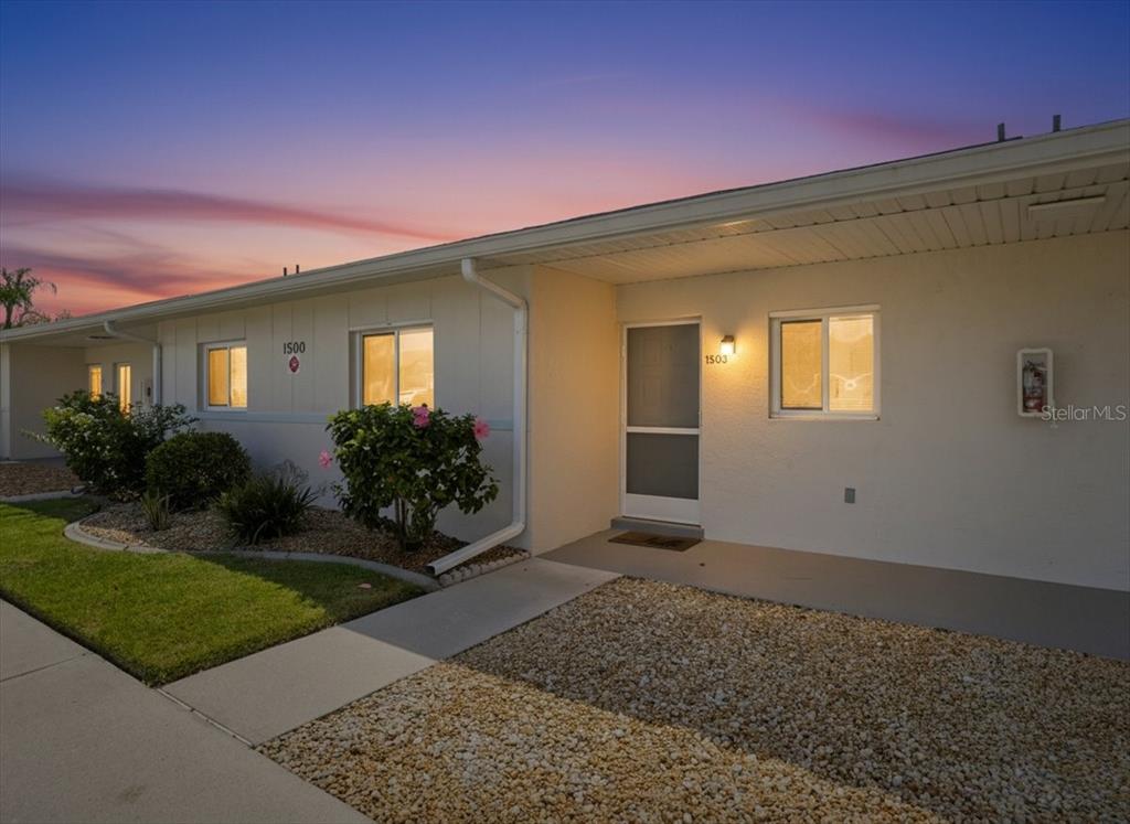 The exterior of a single-story residential building features a walkway, gravel landscaping, and a doorway — 12538 SW KINGSWAY CIRCLE UNIT 1503, LAKE SUZY, FL