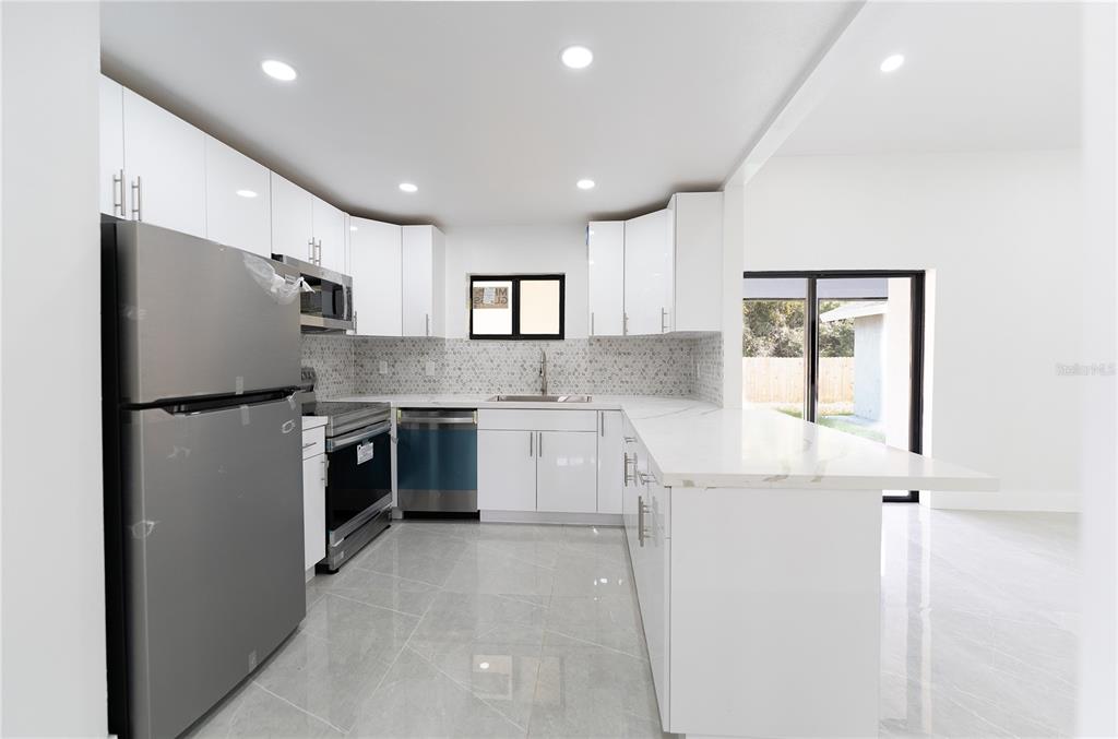 A modern kitchen features white cabinets, stainless steel appliances, and light-colored tile flooring — 848 E FLAG LANE, KISSIMMEE, FL