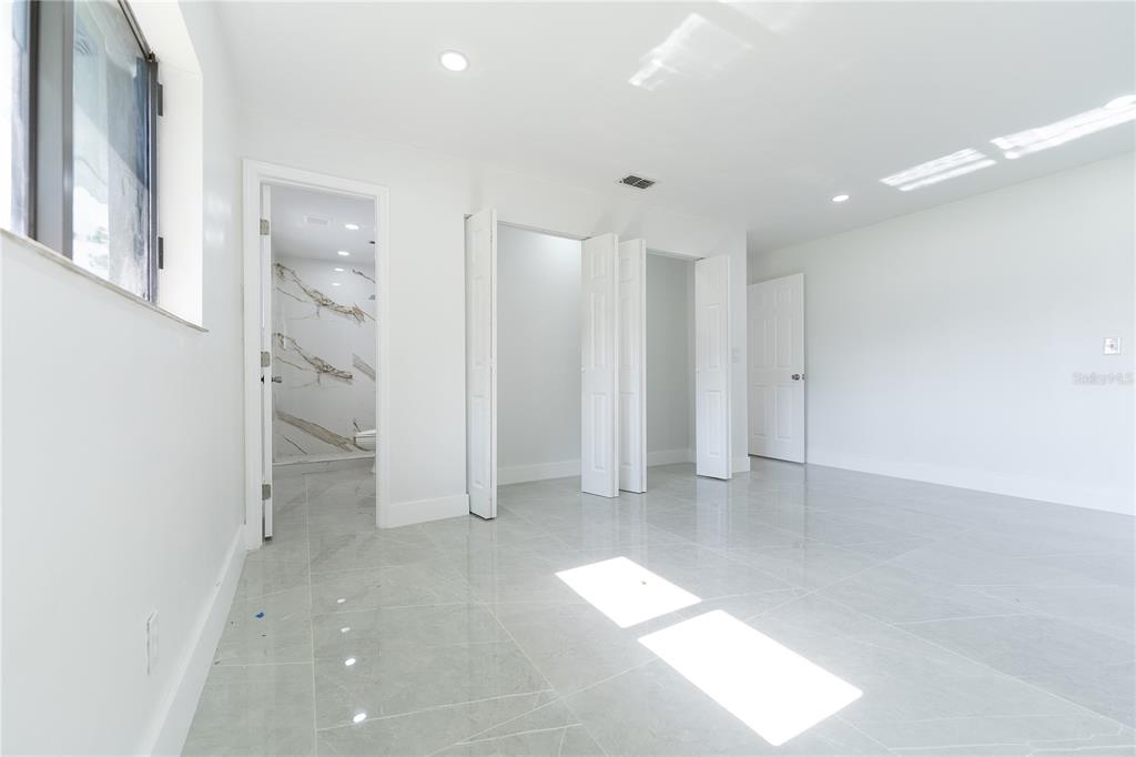 A bright room with light gray tile flooring, white walls, multiple closet doors, and an ensuite bathroom — 848 E FLAG LANE, KISSIMMEE, FL