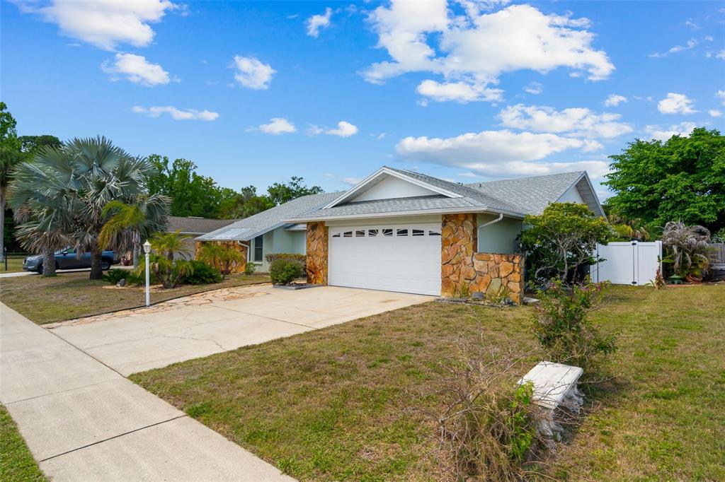 A single-story house with a stone-accented garage and a concrete driveway under a blue sky — 10116 LANDMARK DRIVE, HUDSON, FL