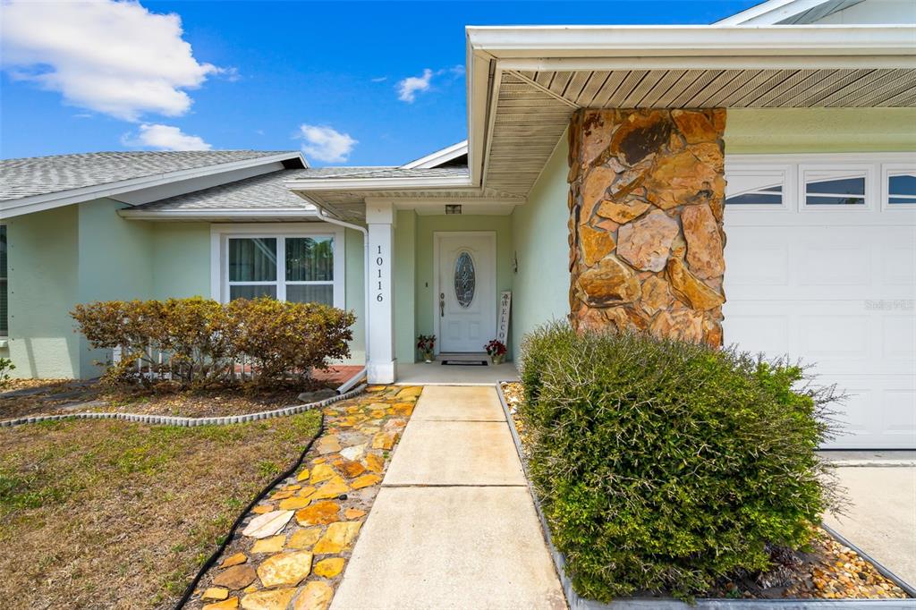 The exterior of a light green house features a stone-accented pillar and a concrete walkway — 10116 LANDMARK DRIVE, HUDSON, FL