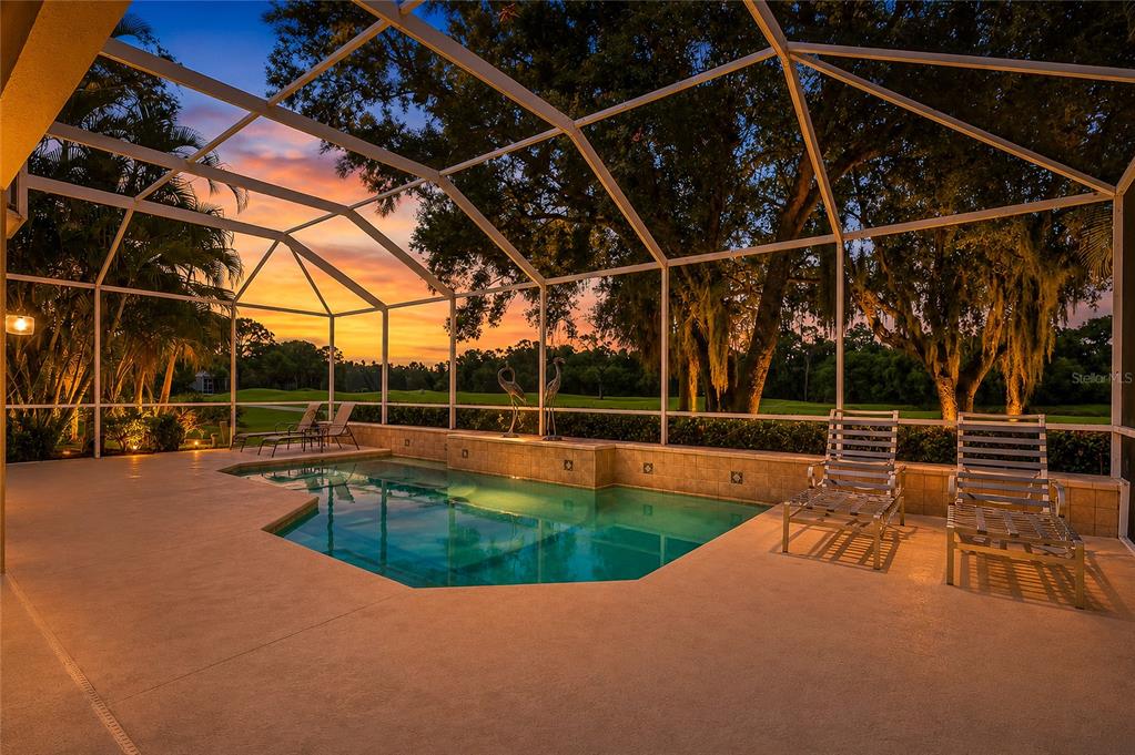 A screened-in swimming pool patio overlooks a golf course at sunset — 8718 54TH AVENUE E, BRADENTON, FL