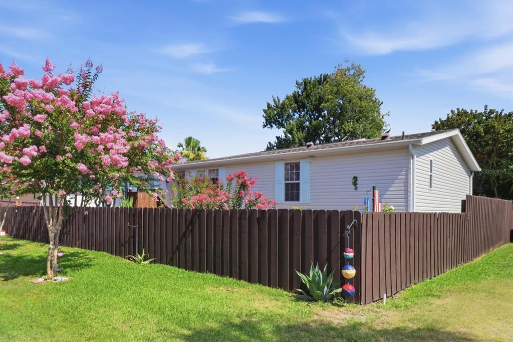 A light-colored house sits behind a brown wooden fence with a blooming pink tree nearby — 8421 W SCOTT COURT, HOMOSASSA, FL