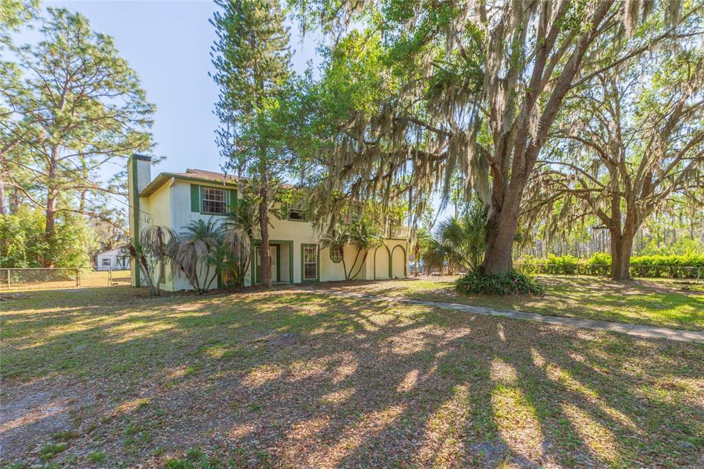 A two-story house with green shutters sits on a grassy lot under large oak trees — 17616 EAGLE LANE, LUTZ, FL