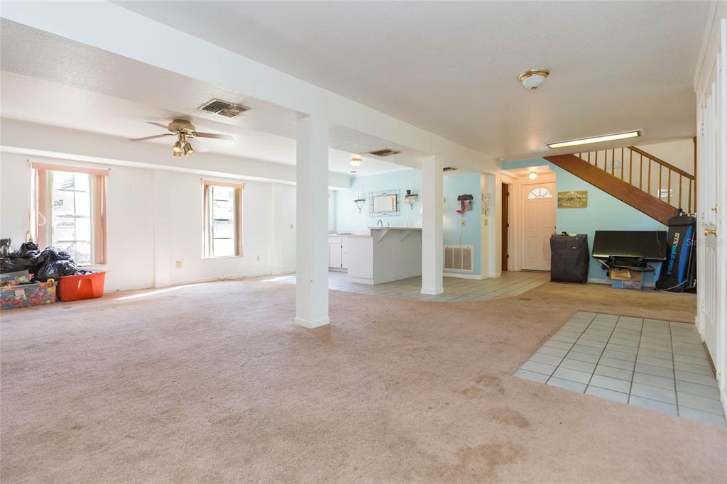 A spacious basement features carpeted flooring, support columns, a small kitchenette, and a wooden staircase — 17616 EAGLE LANE, LUTZ, FL
