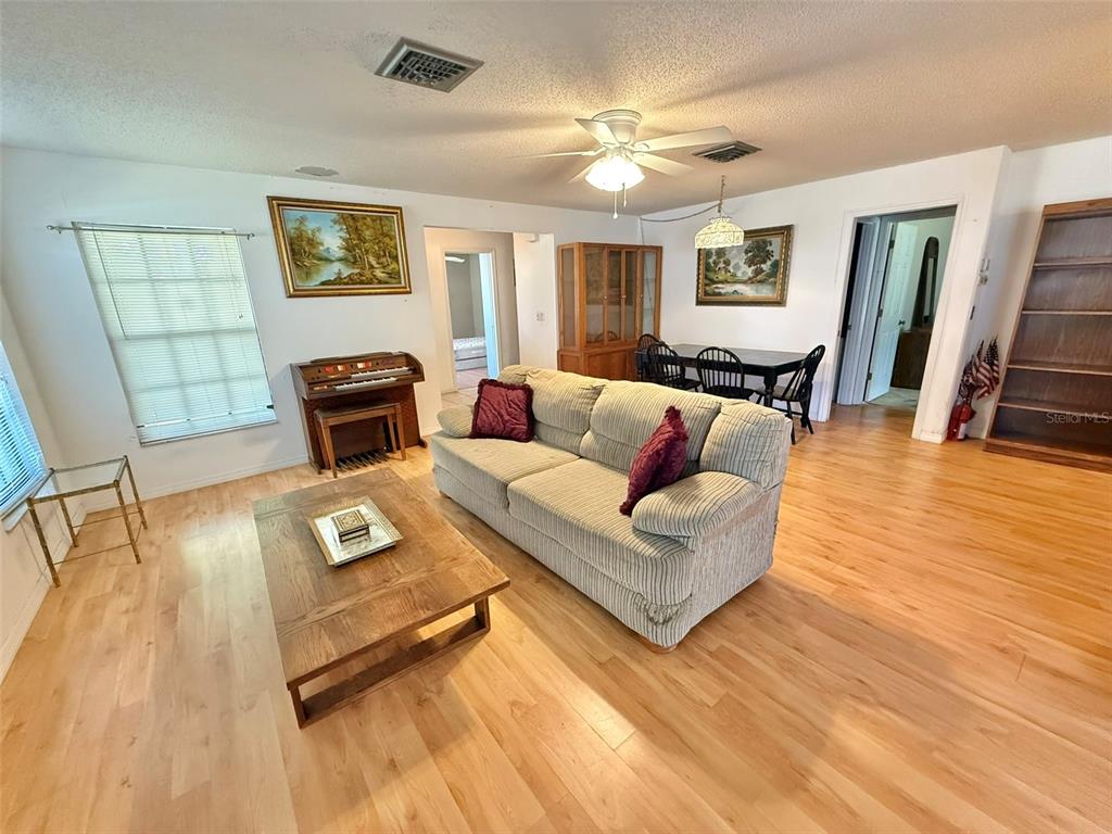 A living room features light wood flooring, a beige sofa, a piano, and dining area — 3112 VIVIENDA BOULEVARD, BRADENTON, FL