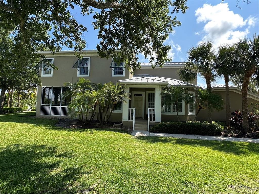 A two-story house with a metal roof, screened porch, and palm trees in the yard — 10600 LEMON CREEK LOOP UNIT 101, ENGLEWOOD, FL
