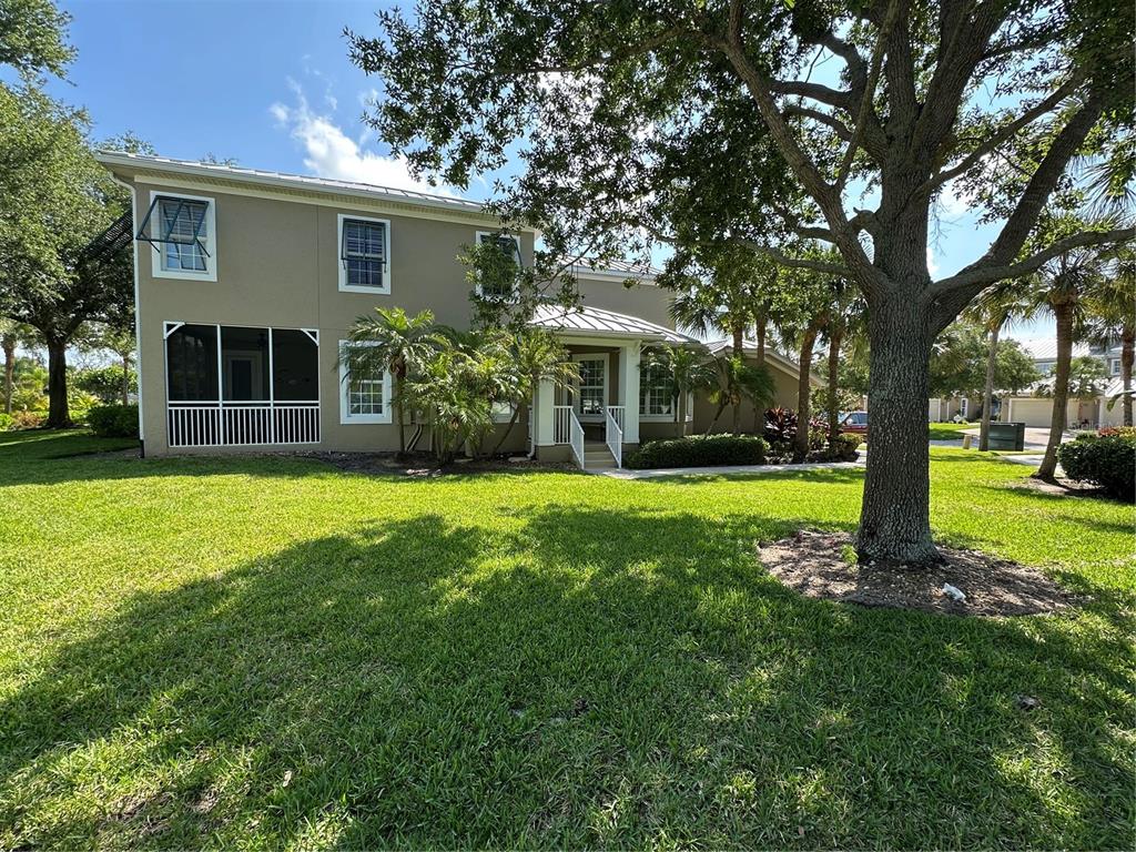 A two-story house with a screened-in porch, metal roof, and large oak tree in front — 10600 LEMON CREEK LOOP UNIT 101, ENGLEWOOD, FL