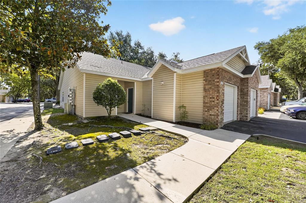 A tan-sided house with a brick-accented garage and a concrete walkway leading to the entrance — 4700 SW ARCHER ROAD UNIT S-127, GAINESVILLE, FL