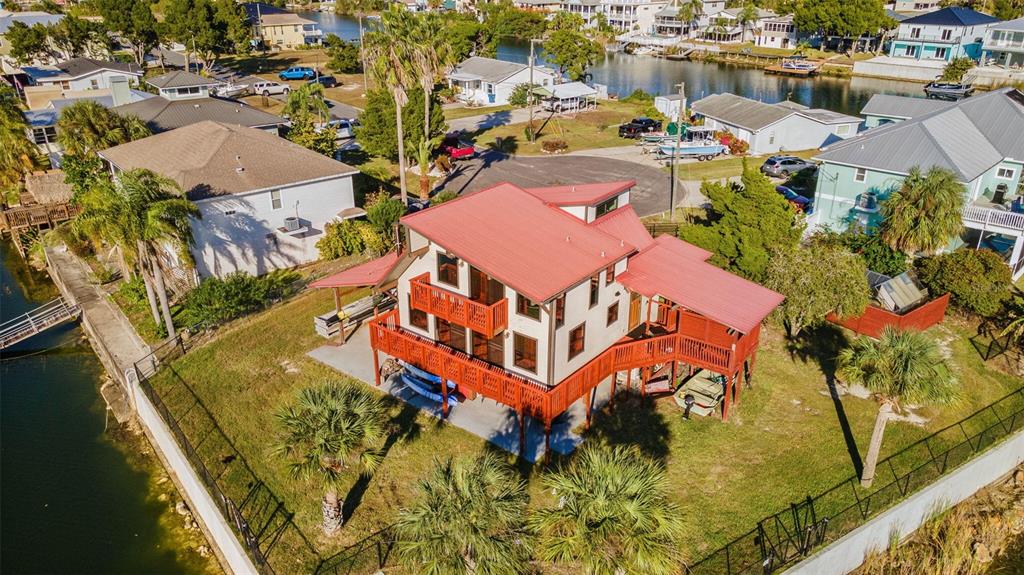 An elevated house with a red metal roof sits on a waterfront lot with palm trees — 3179 AZALEA DRIVE, HERNANDO BEACH, FL
