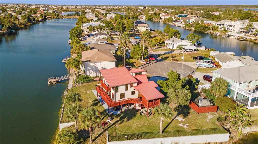 An elevated house with a red metal roof sits on a waterfront lot with docks — 3179 AZALEA DRIVE, HERNANDO BEACH, FL