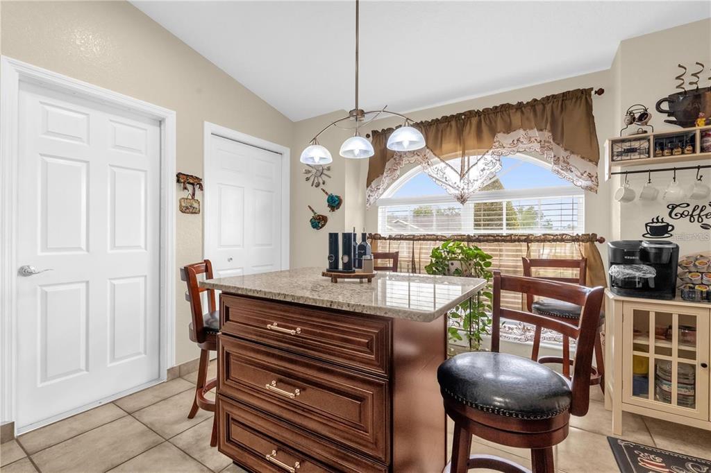A kitchen breakfast nook features a granite-topped island, bar stools, and a window with valances — 1366 MERRIMACK PLACE, DAVENPORT, FL