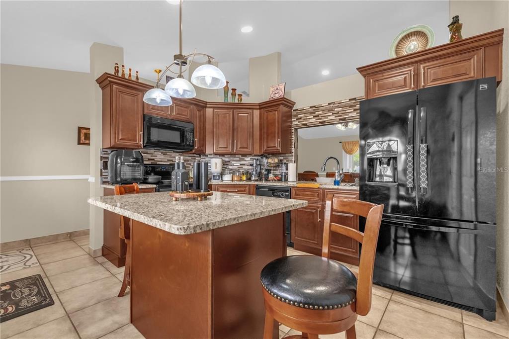 A kitchen features dark wood cabinets, granite countertops, a center island, and a black refrigerator — 1366 MERRIMACK PLACE, DAVENPORT, FL