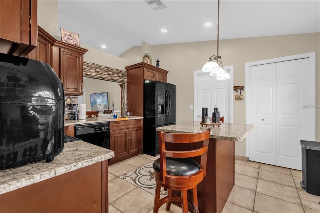 A kitchen features dark wood cabinets, granite countertops, a center island, and tile flooring — 1366 MERRIMACK PLACE, DAVENPORT, FL