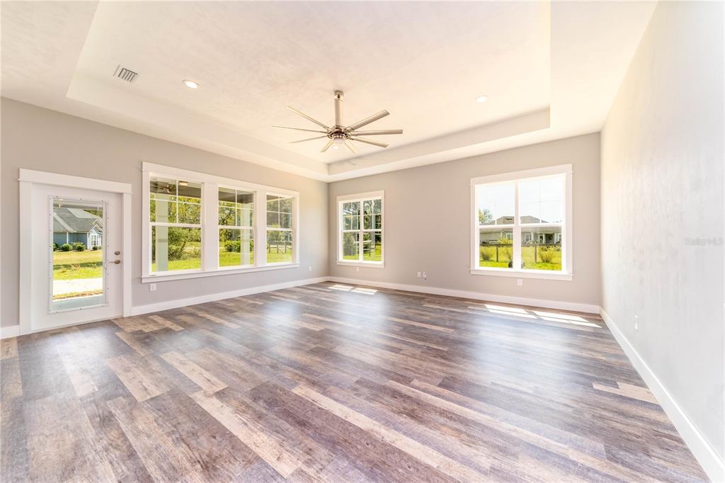 A bright, empty room features wood-look flooring, a tray ceiling with a fan, and large windows — TBD2 71ST LANE, O'BRIEN, FL