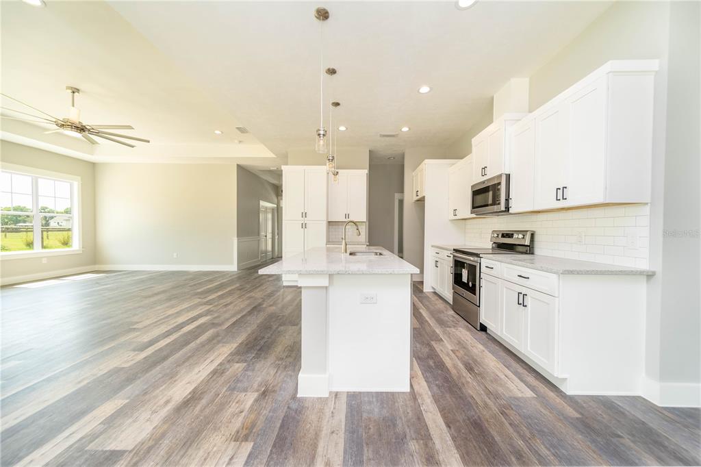 A modern kitchen features white cabinets, a granite-topped island, and wood-look flooring — TBD2 71ST LANE, O'BRIEN, FL