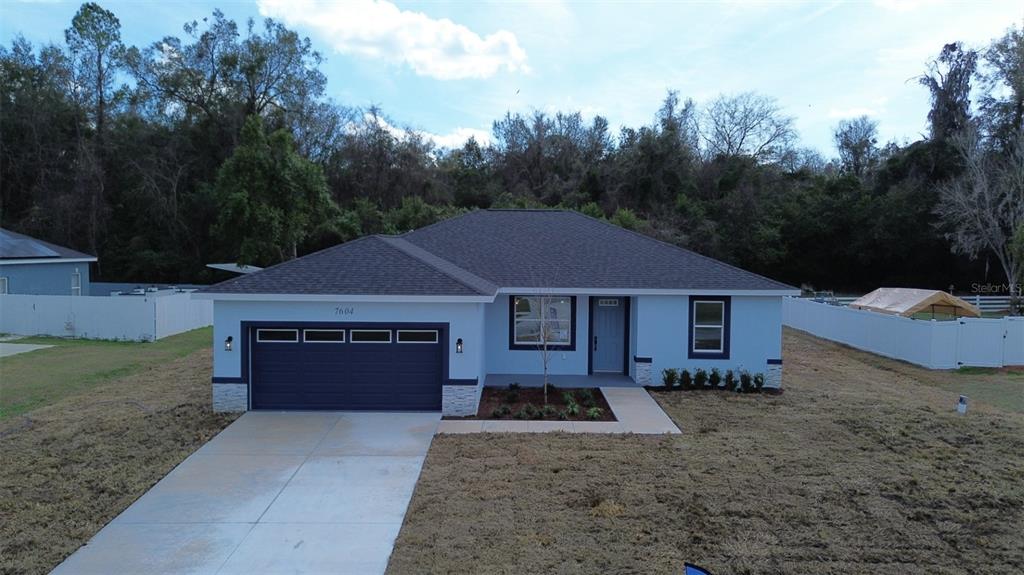 A light blue single-story house features a dark garage door and a concrete driveway — 7604 SW 103RD LOOP, OCALA, FL
