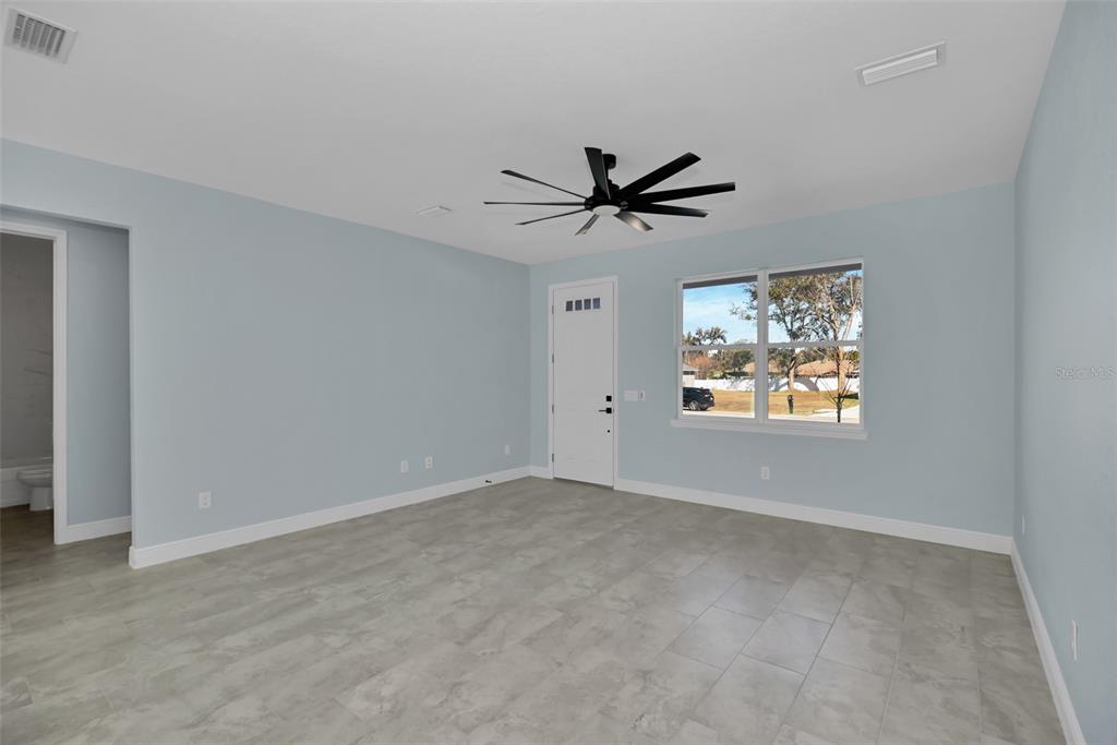 A room with light blue walls, gray tile flooring, a ceiling fan, and a white door — 7604 SW 103RD LOOP, OCALA, FL