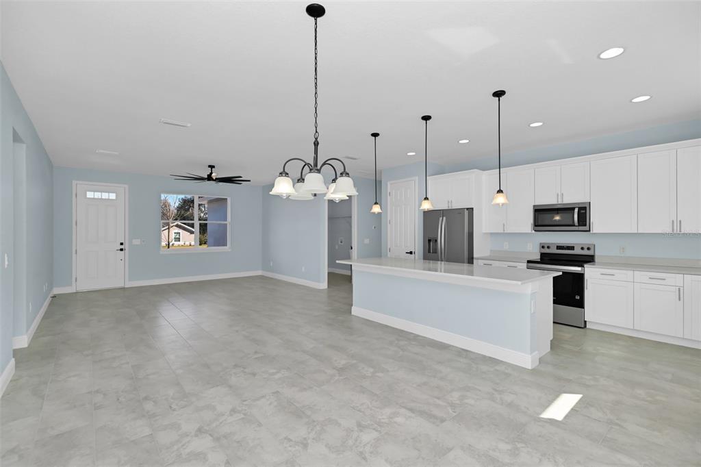 A kitchen with white cabinets and a breakfast bar opens into a light blue room — 7604 SW 103RD LOOP, OCALA, FL