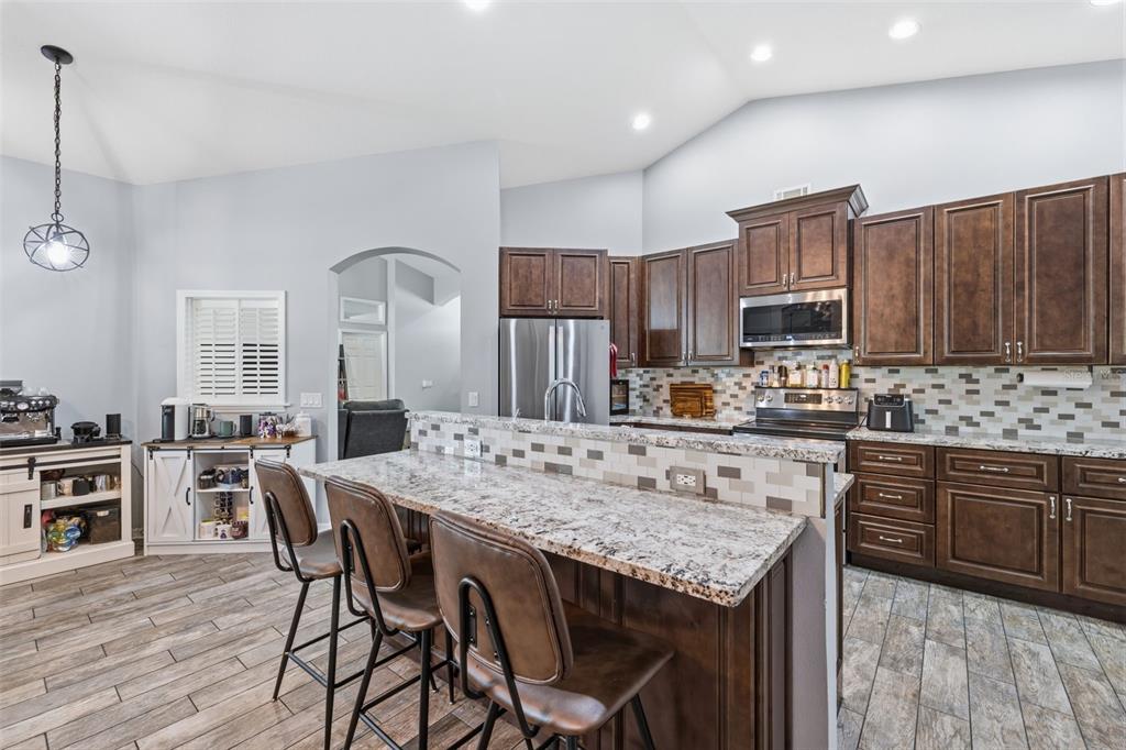 A kitchen features dark wood cabinets, granite countertops, a breakfast bar, and light tile flooring — 12020 RUNNING FOX CIRCLE, RIVERVIEW, FL
