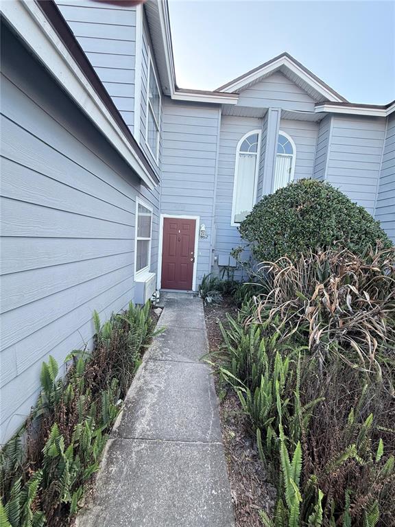 A concrete walkway leads to the red front door of a light blue house exterior — 862 CARIBBEAN DRIVE, DAVENPORT, FL