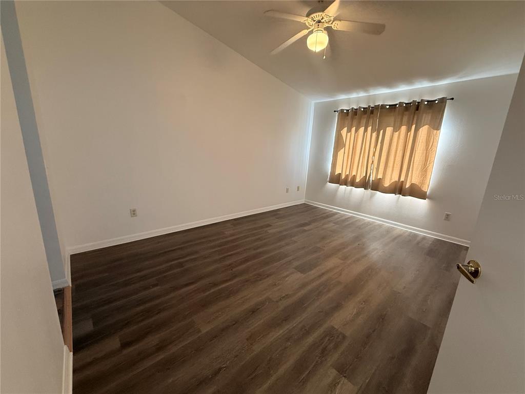 An empty bedroom features wood-look flooring, white walls, a ceiling fan, and window curtains — 862 CARIBBEAN DRIVE, DAVENPORT, FL
