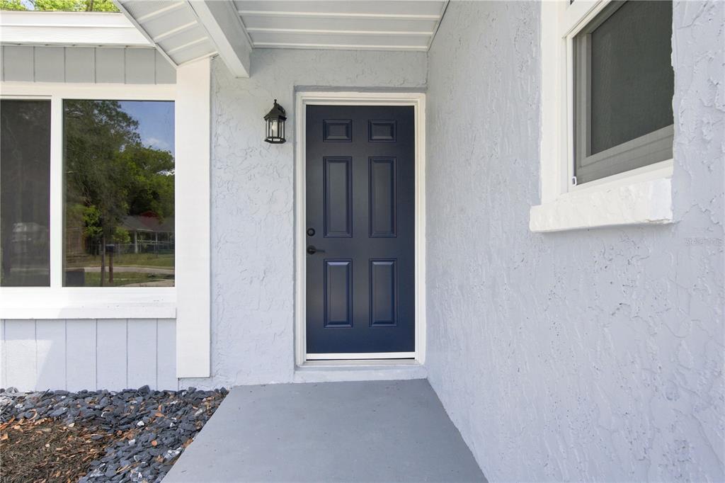 A dark blue front door is centered on a light blue stucco porch — 7033 WENTWORTH WAY, NEW PORT RICHEY, FL