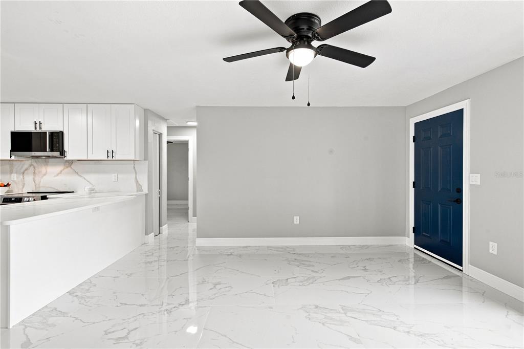 A kitchen and dining area with white cabinets, marble-look tile floors, and a blue door — 7033 WENTWORTH WAY, NEW PORT RICHEY, FL