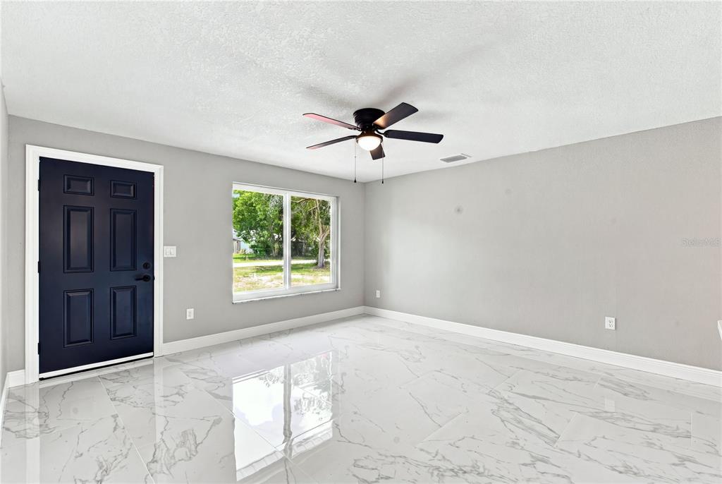 An empty room features gray walls, white marble-look tile flooring, a ceiling fan, and a door — 7033 WENTWORTH WAY, NEW PORT RICHEY, FL