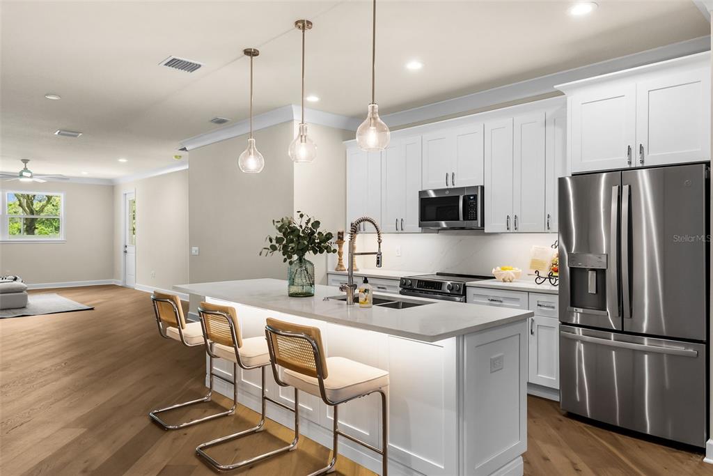 A modern kitchen features white cabinetry, a quartz island with bar seating, and stainless steel appliances — 207 ATHENIAN WAY, TARPON SPRINGS, FL