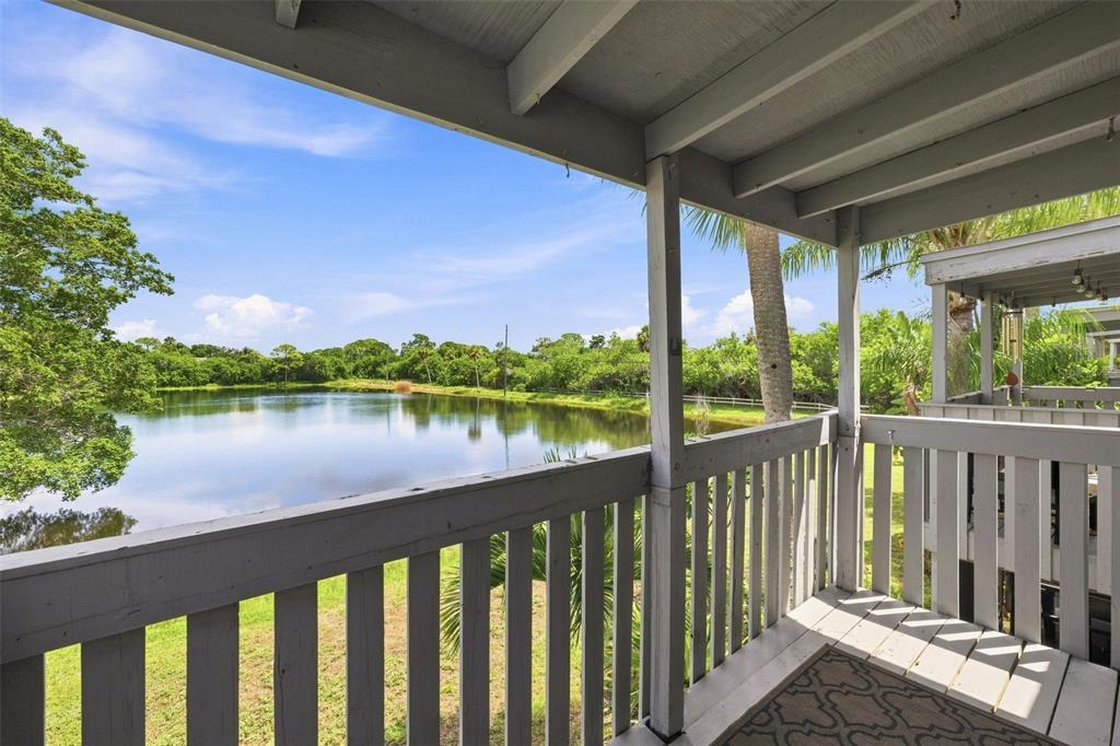 A wooden balcony overlooks a calm pond surrounded by lush green trees under a blue sky — 11409 8TH STREET N UNIT 1504, ST PETERSBURG, FL