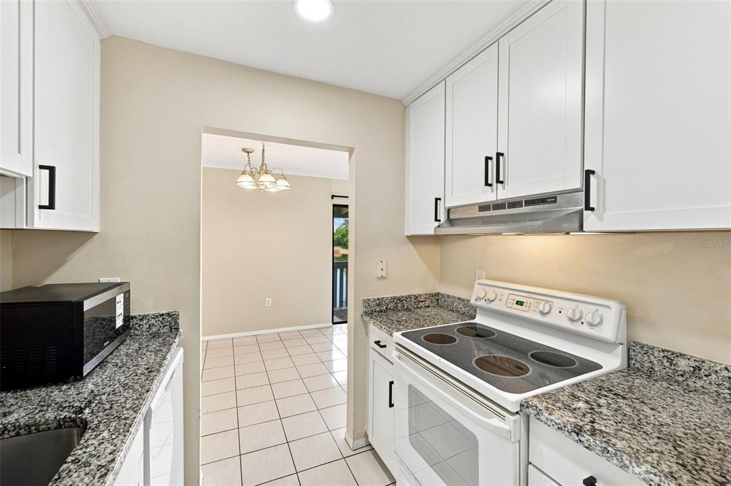 A kitchen with white cabinets, granite countertops, and a white electric stove leads to a dining area — 11409 8TH STREET N UNIT 1504, ST PETERSBURG, FL