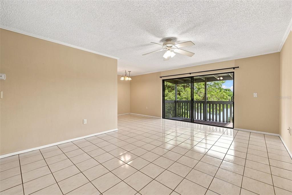 An empty room with beige walls, white tile flooring, a ceiling fan, and sliding glass doors — 11409 8TH STREET N UNIT 1504, ST PETERSBURG, FL