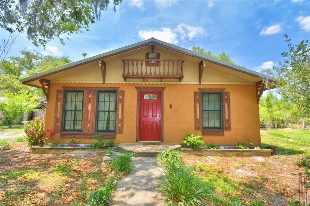 A single-story house with tan stucco walls, a red front door, and a wooden balcony — 760 MCCLELLAN ROAD, FROSTPROOF, FL