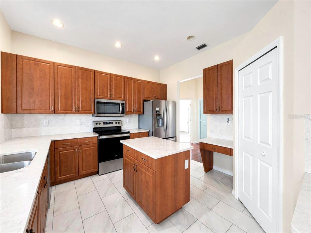 A kitchen features wood cabinets, stainless steel appliances, a center island, and white countertops — 4775 8TH STREET NE, NAPLES, FL