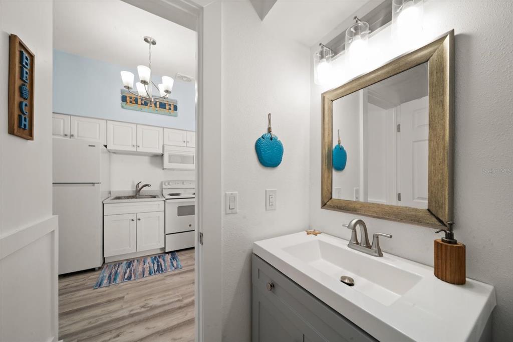 A bathroom vanity with a gray cabinet and white sink sits in front of a kitchen — 711 E GULF BOULEVARD, INDIAN ROCKS BEACH, FL