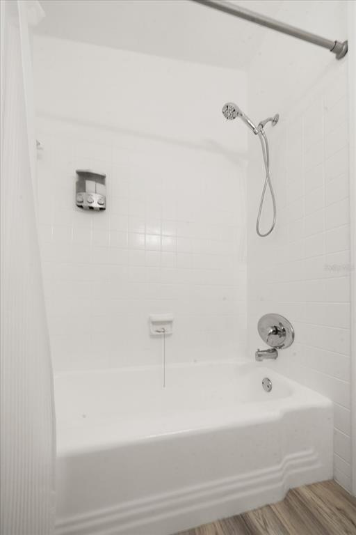 A white tiled bathtub and shower combination with a handheld showerhead and wall-mounted soap dispenser — 711 E GULF BOULEVARD, INDIAN ROCKS BEACH, FL