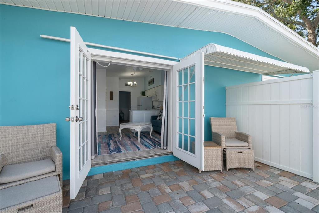 A patio with wicker chairs leads through French doors into a furnished living room — 711 E GULF BOULEVARD, INDIAN ROCKS BEACH, FL