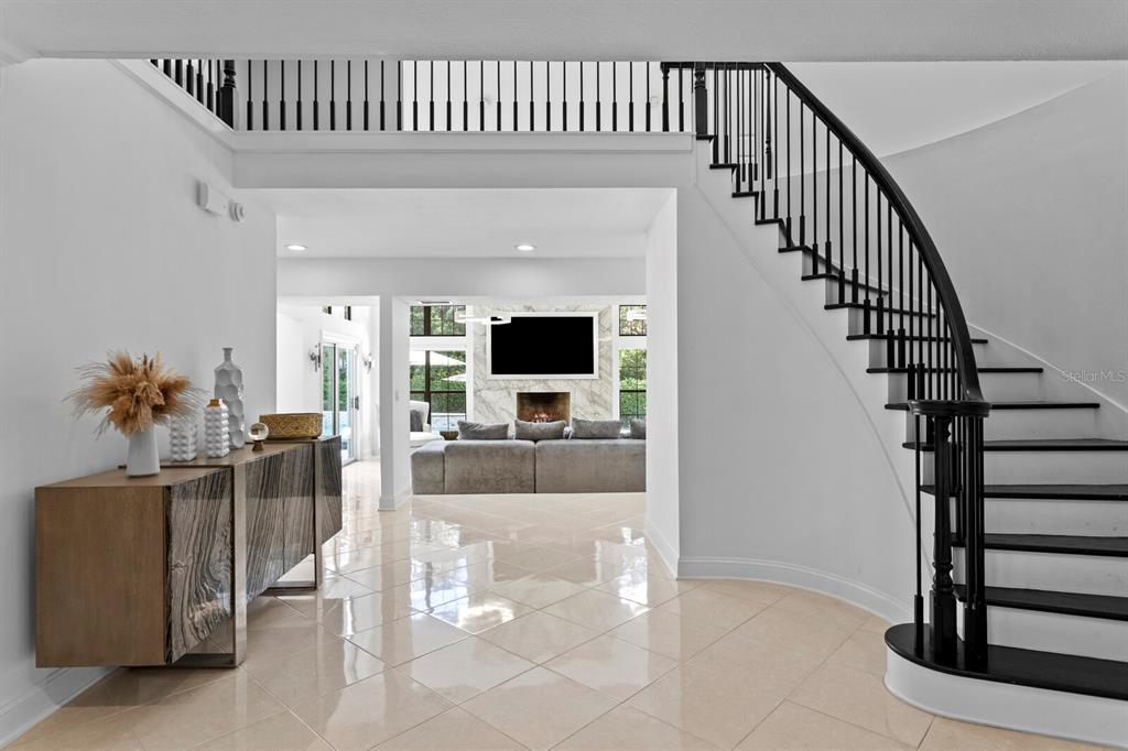 A foyer with a curved staircase leads to a living room featuring a fireplace — 1001 BAJADA DE AVILA, TAMPA, FL